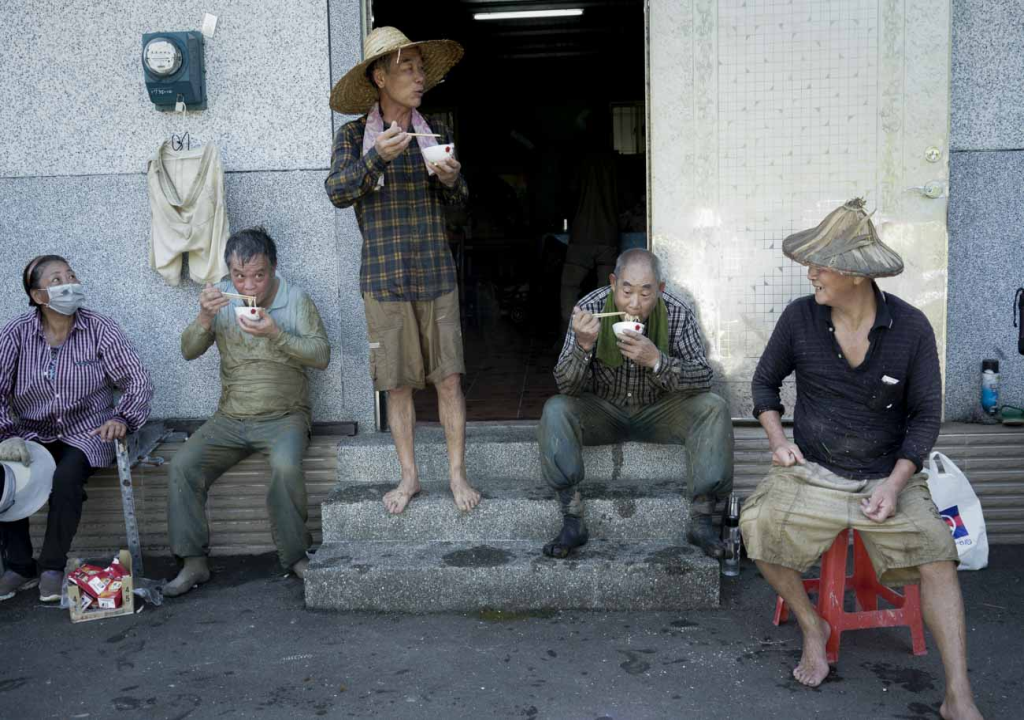 農友們從清晨五點多割到上午十點多，已經割了一大半，簡秋陽（右）招呼大家吃點心休息一下，由於換工割稻需要大量人力，也非常消耗體力，需要大量的食物補充體力，因此，吃「割稻仔飯」是割稻當天非常慎重的大事！簡秋陽準備豐盛菜飯招待換工農友，也藉此表達謝意。 圖：張良一/攝