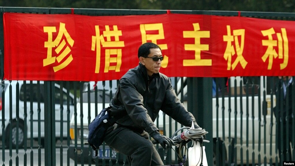 一名北京男子騎車從敦促市民積極參加地方選舉的標語前路過。圖/美國之音資料照片