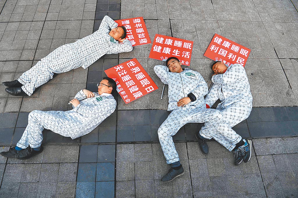 中國年輕人近日刮起「躺平主義」旋風，在網路上引發巨大反響。圖為重慶鼾友會的幾位成員身穿睡衣，手上拿著睡眠相關標語的牌子躺在街頭。（中新社）